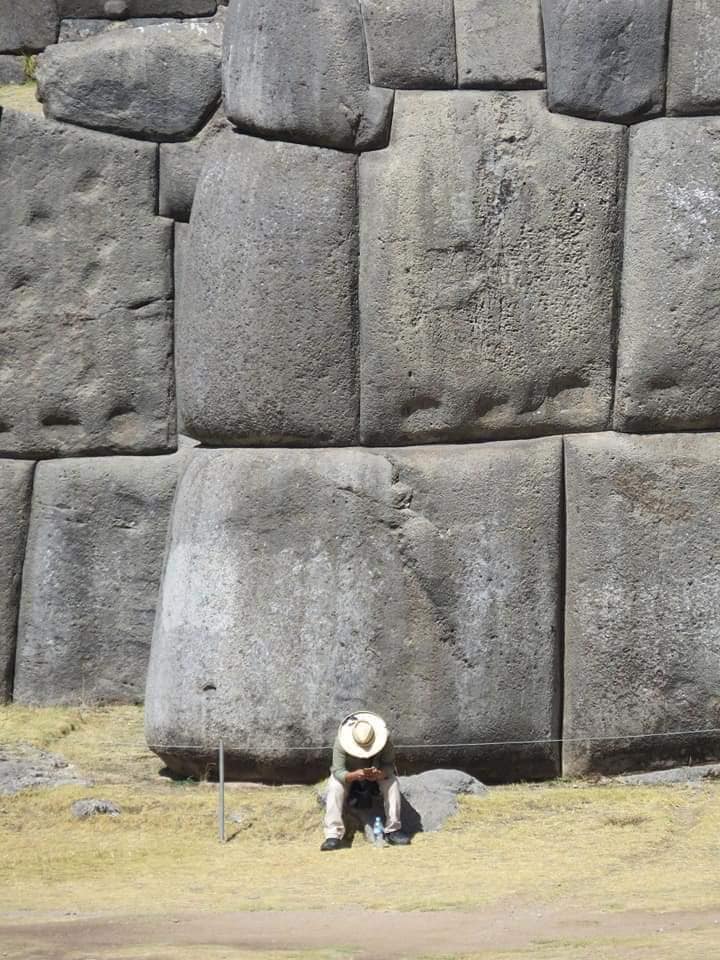 A man sitting next to a massive stone at Sacsayhuaman.